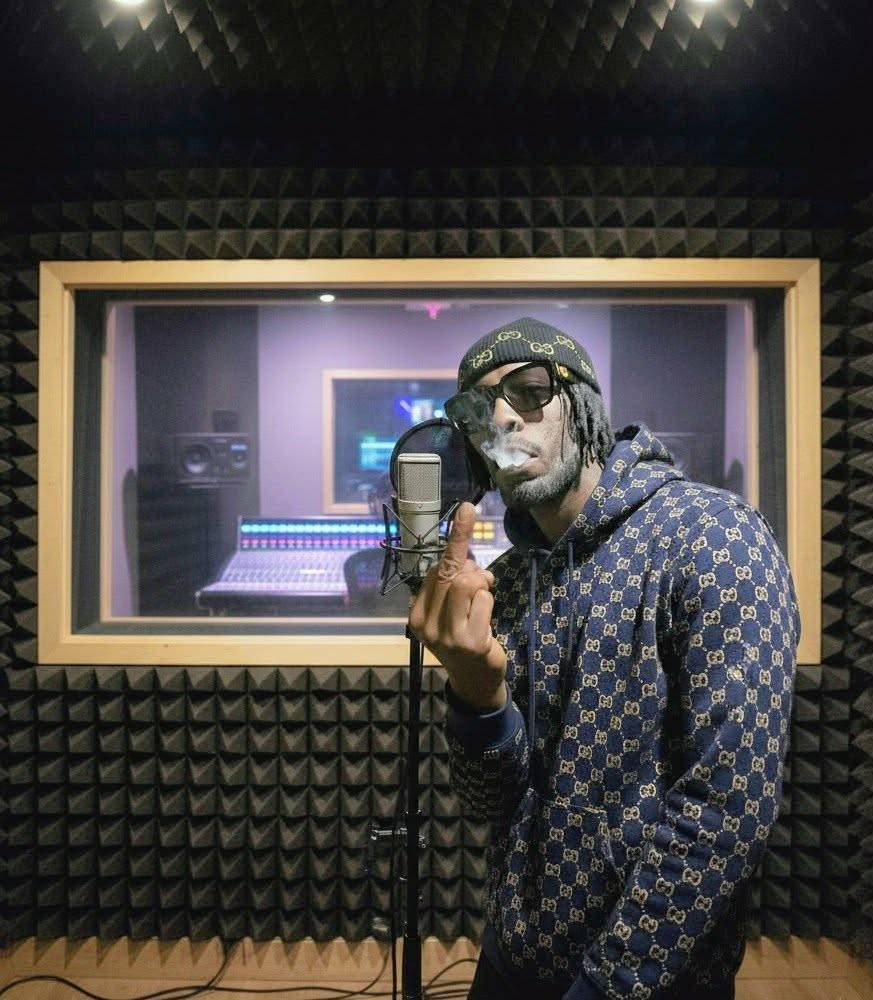 MINDBENDA in a Gucci-patterned beanie and hoodie recording vocals in a sound booth