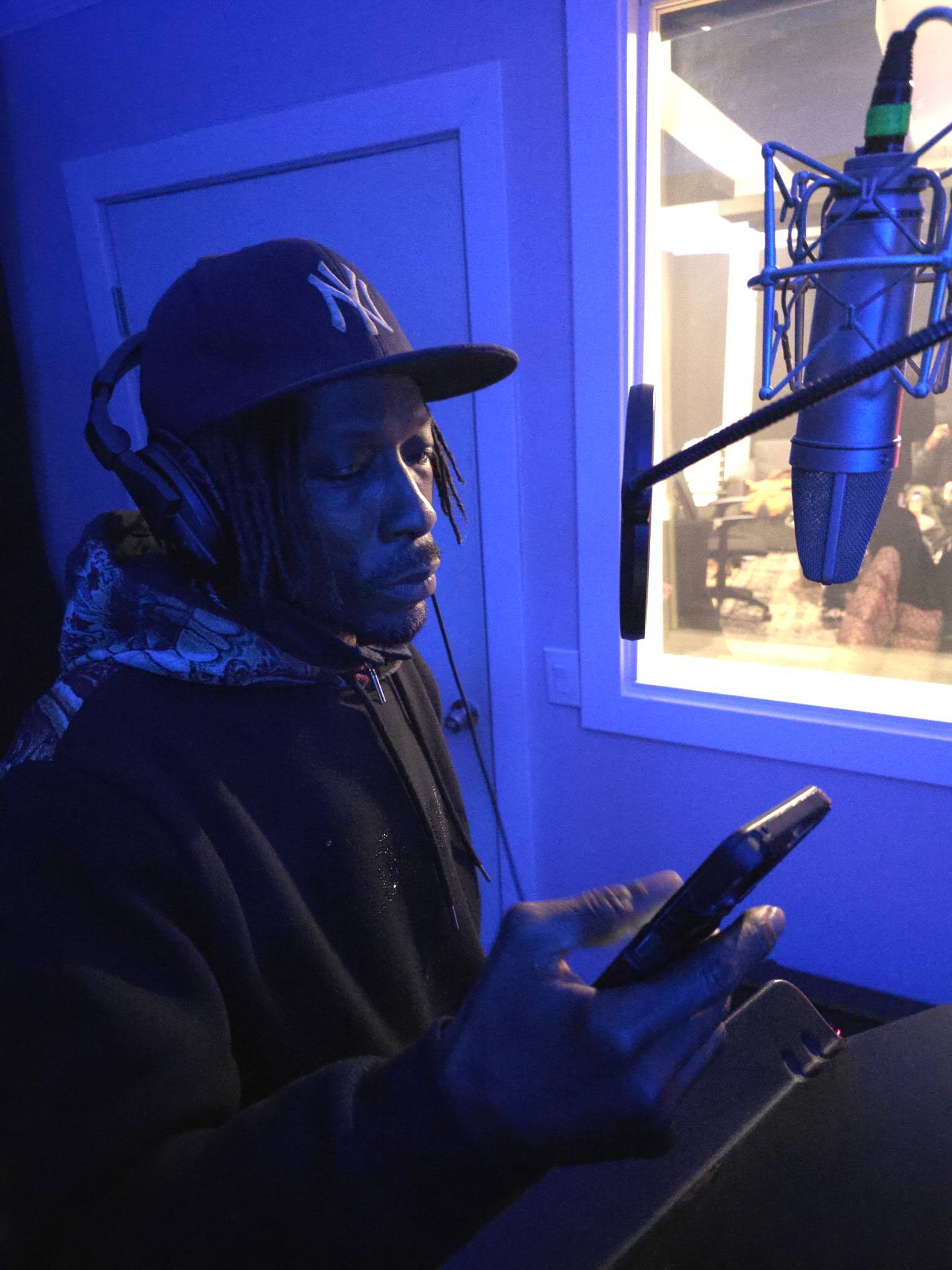MINDBENDA in an NY cap and headphones at the studio microphone in blue light